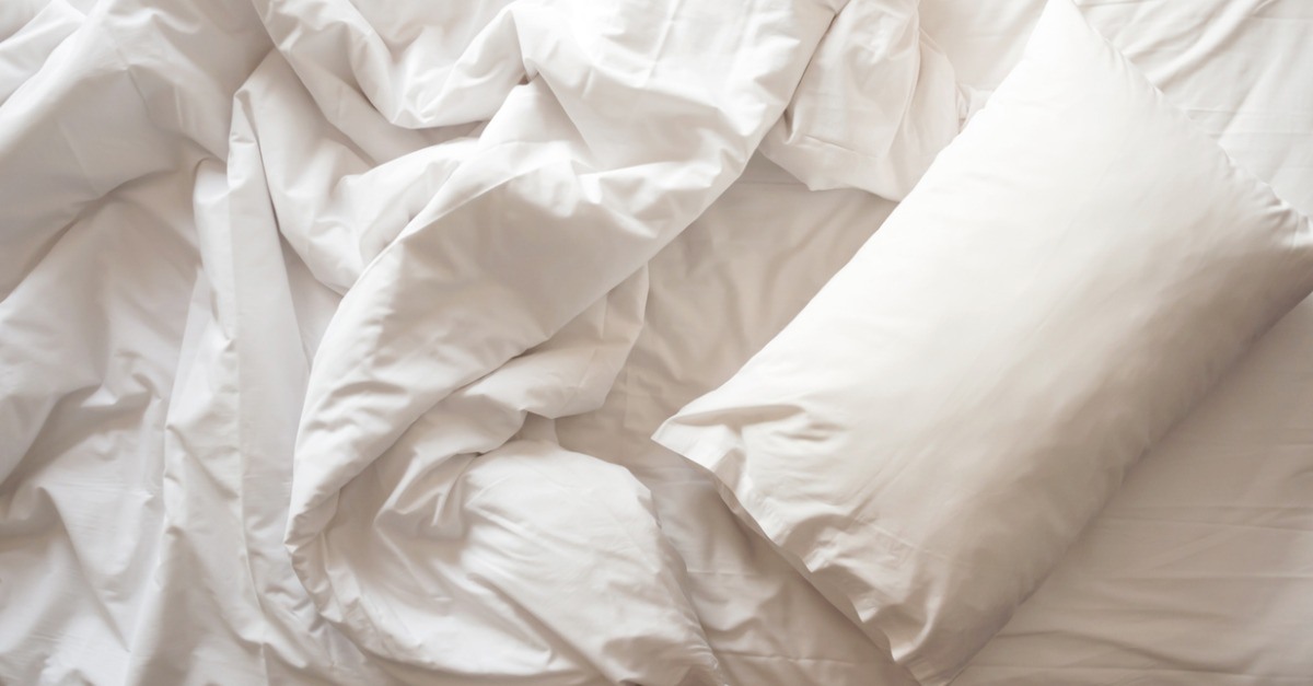 Top view of a messy bed with a white pillow with blankets.